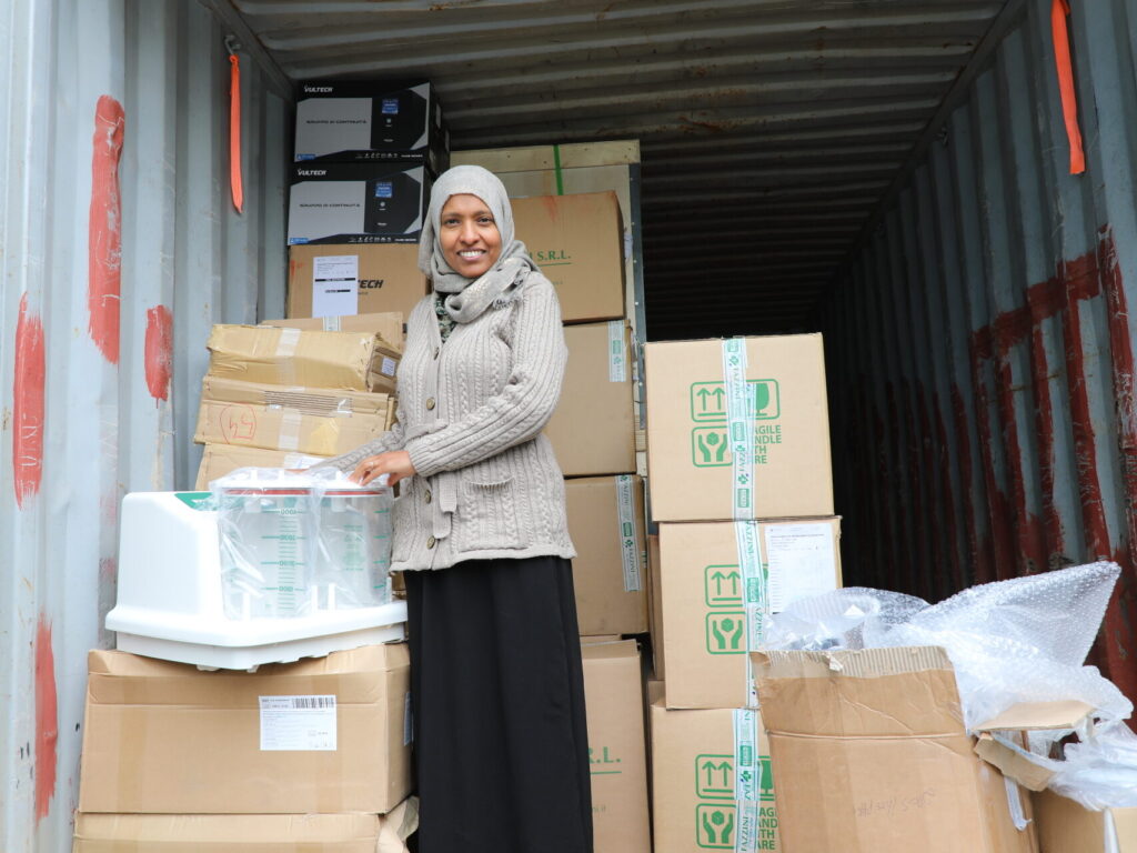 A woman stands smiling between the stacked boxes in a shipping container.