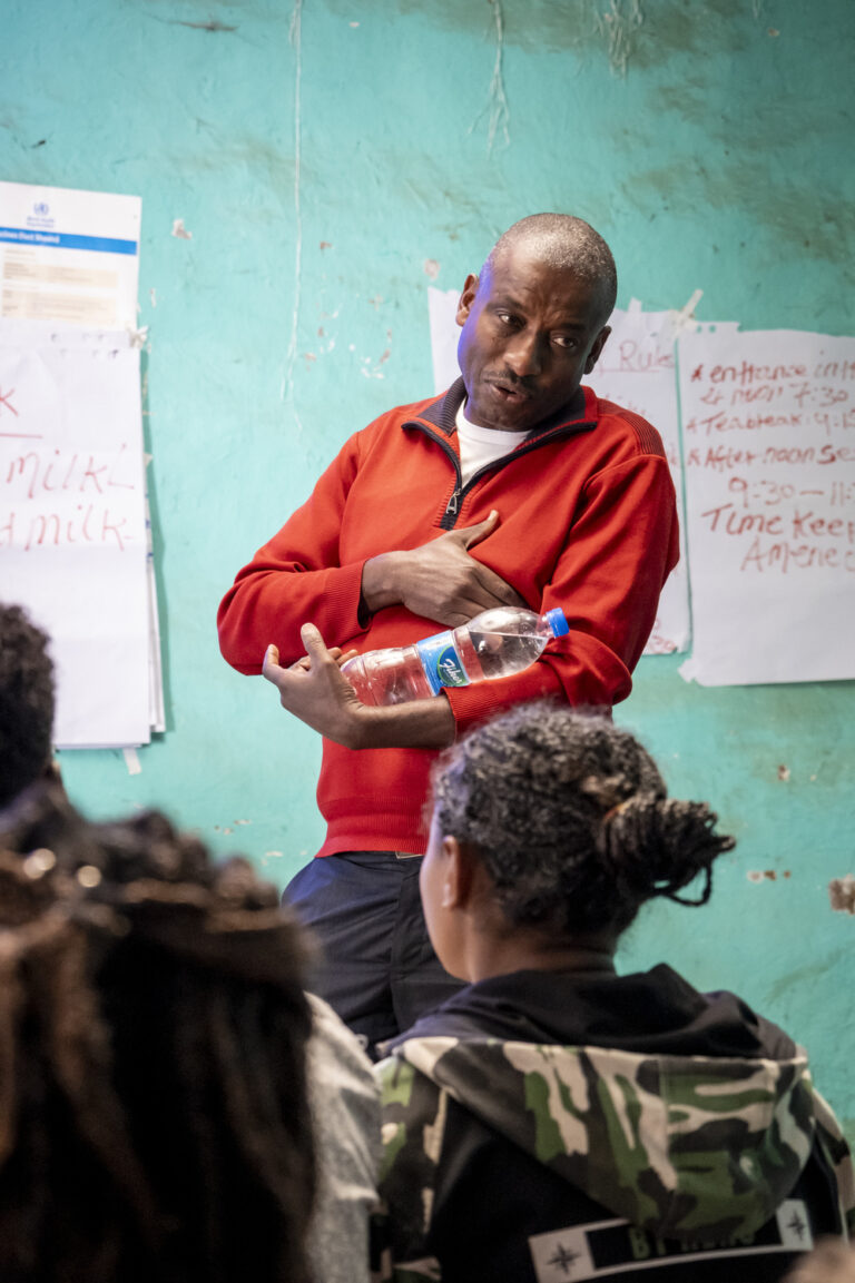 Gojole Goa demonstrating breastfeeding with a plastic water bottle in his arms.