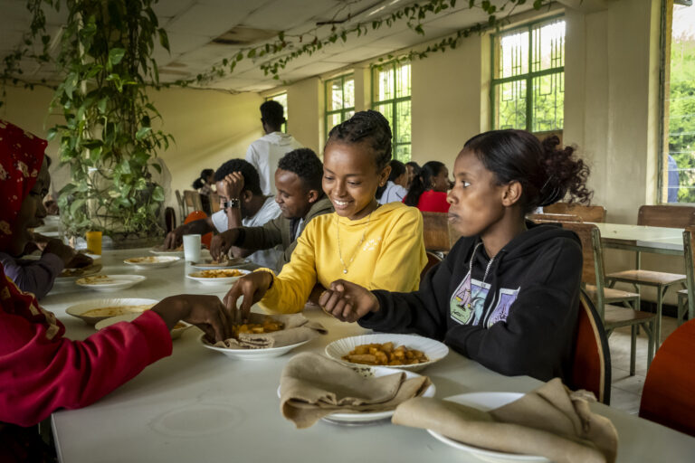 Young students chatting over lunch in a cafeteria surrounded by plants.