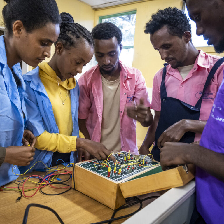 A teacher is teaching two students electronics