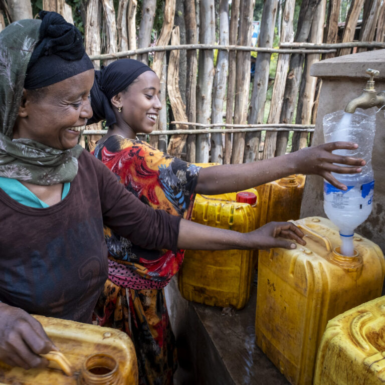 Two women are filling clean drinking water into yellow water canisters.