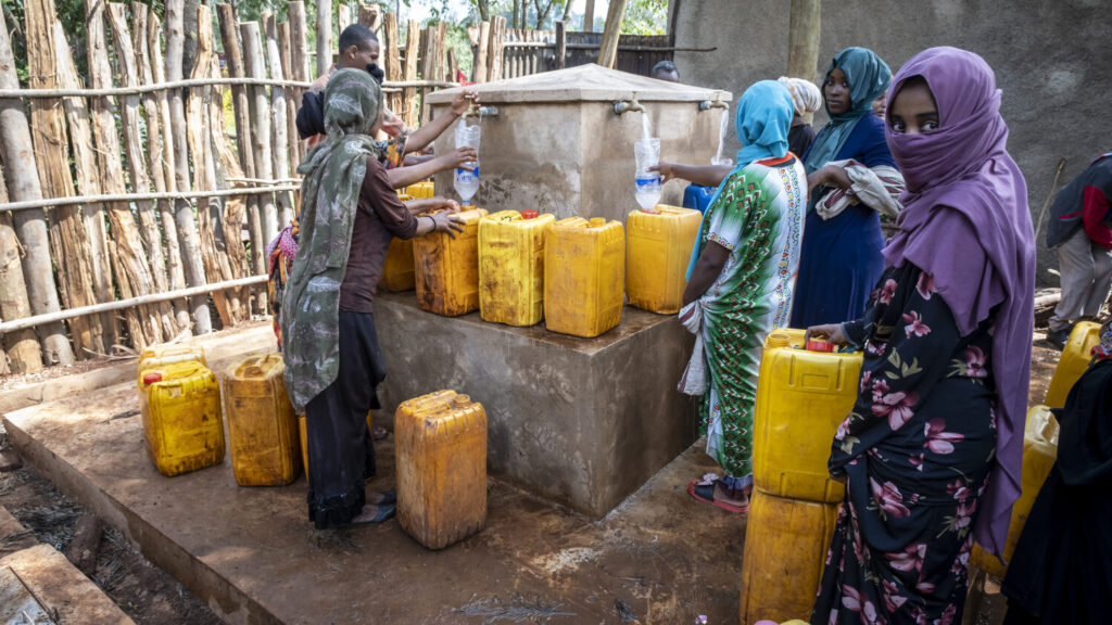 Women are waiting at the water point with their water containers.