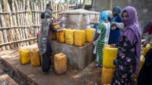 Women are waiting at the water point with their water containers.