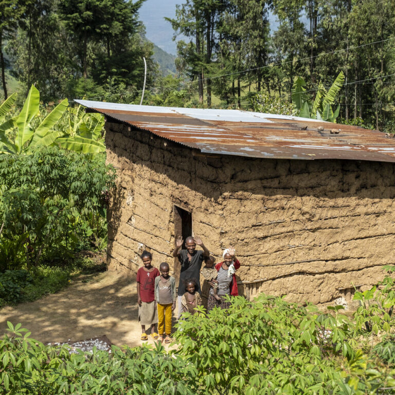 A family stands in front of their home, surrounded by trees and other plants.