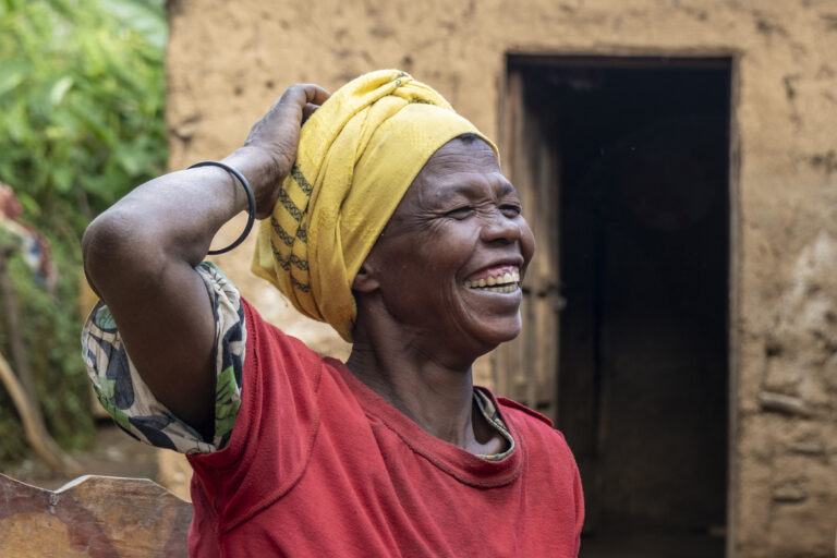 A smiling woman wearing a yellow headscarf and a red shirt outdoors.