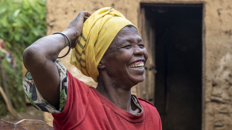 A smiling woman wearing a yellow headscarf and a red shirt outdoors.