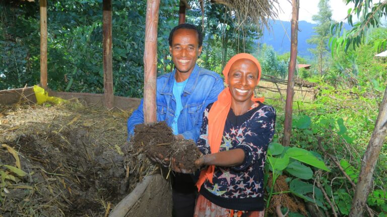 A woman and a man smiling while holding soil toward the camera.