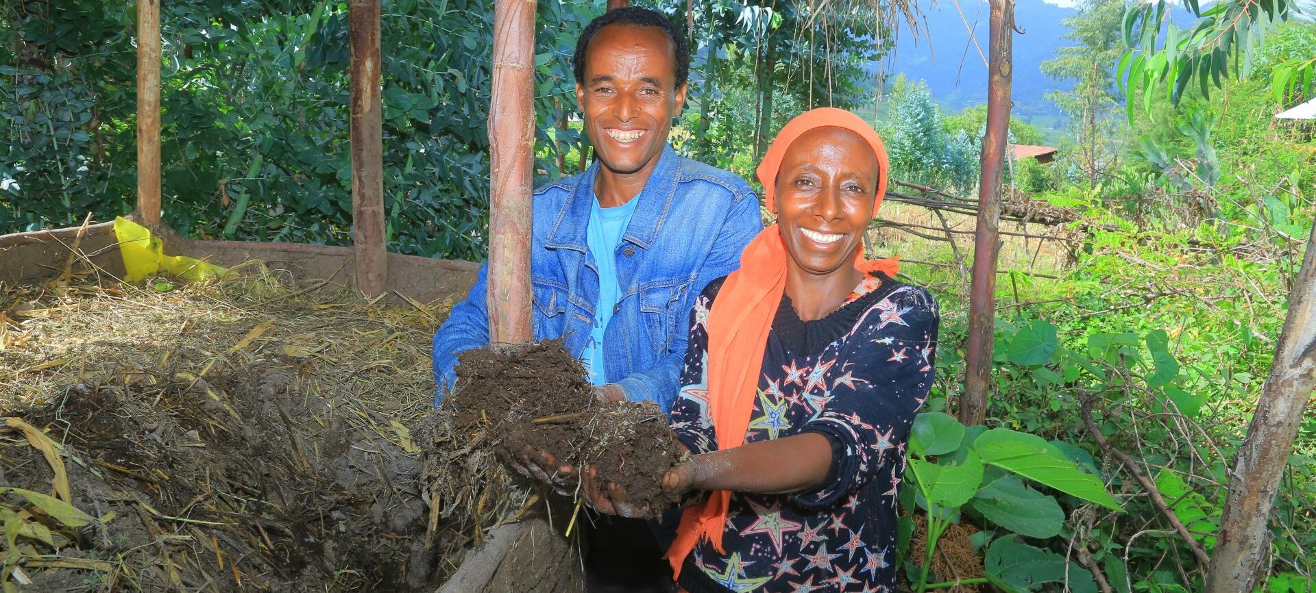 A woman and a man smiling while holding soil toward the camera.
