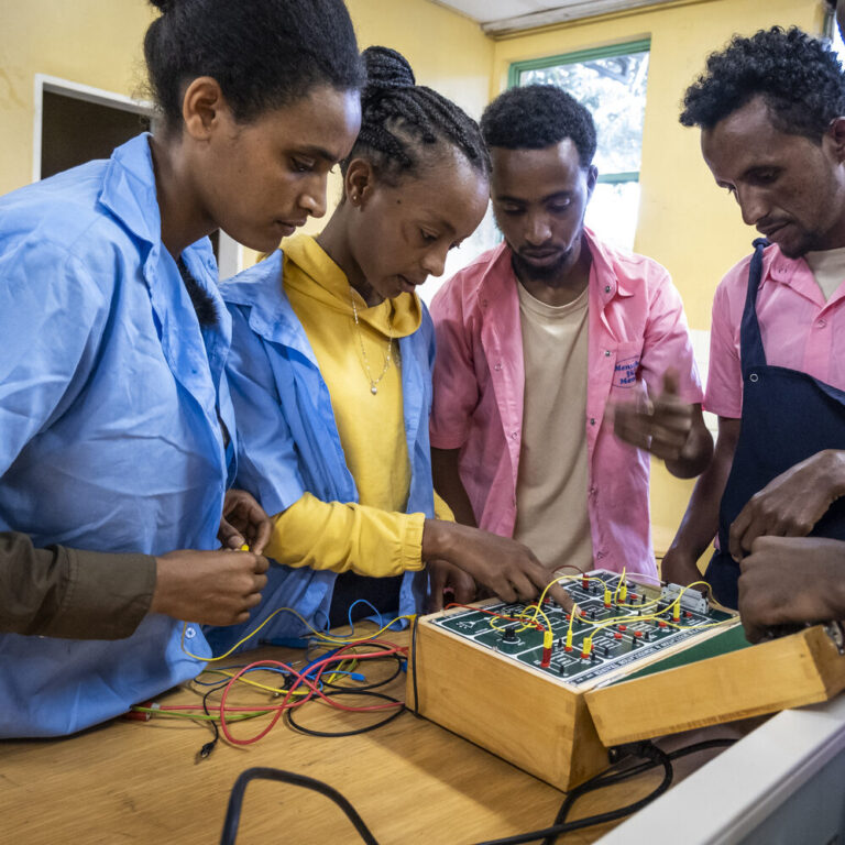 A teacher is teaching two students electronics