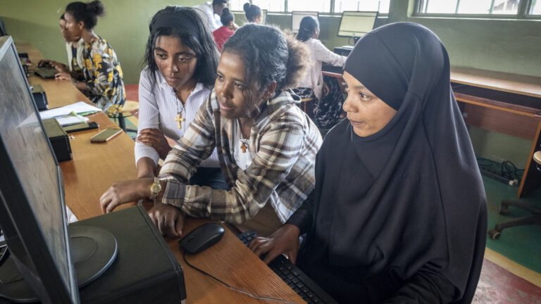 Three young women sharing a computer in a training centre.
