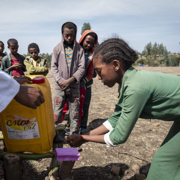 Children are washing their hands with clean water from a yellow canister.