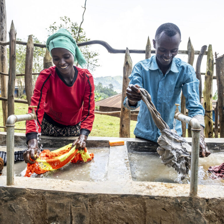 A woman and a man washing clothes at a sink.