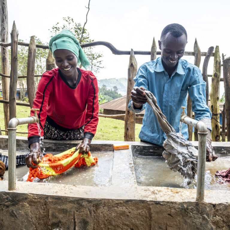 A woman and a man washing clothes at a sink.